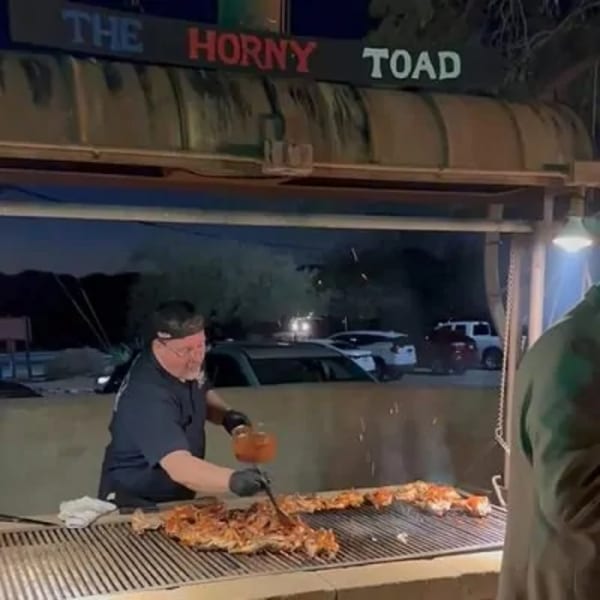 A chef at The Horny Toad restaurant grills large cuts of meat on an outdoor grill at night.