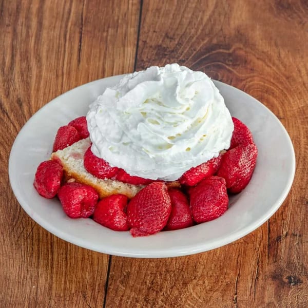 Strawberry shortcake with whipped cream on a white plate, on a wooden table.