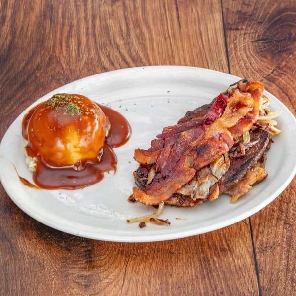 A plate of bacon-wrapped meatloaf with gravy and a side of mashed potatoes on a wooden table.
