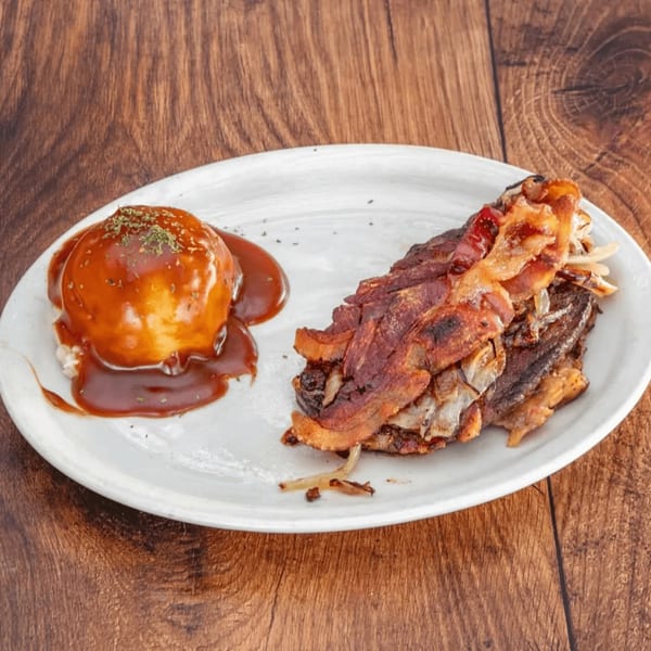 A plate of bacon-wrapped steak with caramelized onions and a side of mashed potatoes with gravy.