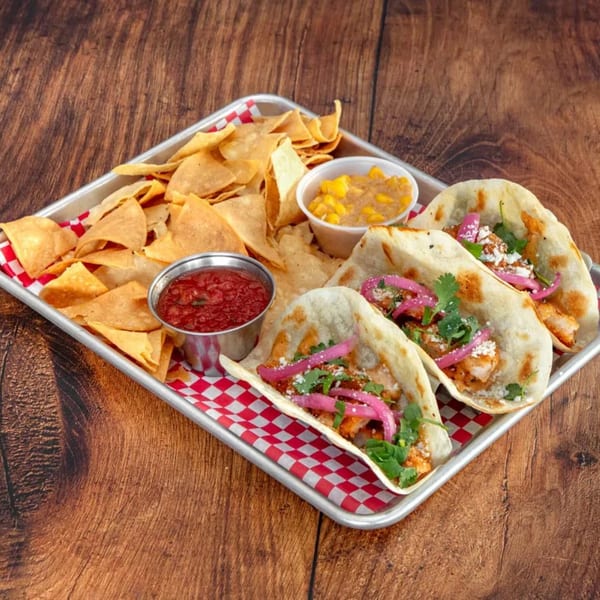 Three tacos with pickled onions and cilantro, tortilla chips, salsa, and corn relish on a tray.