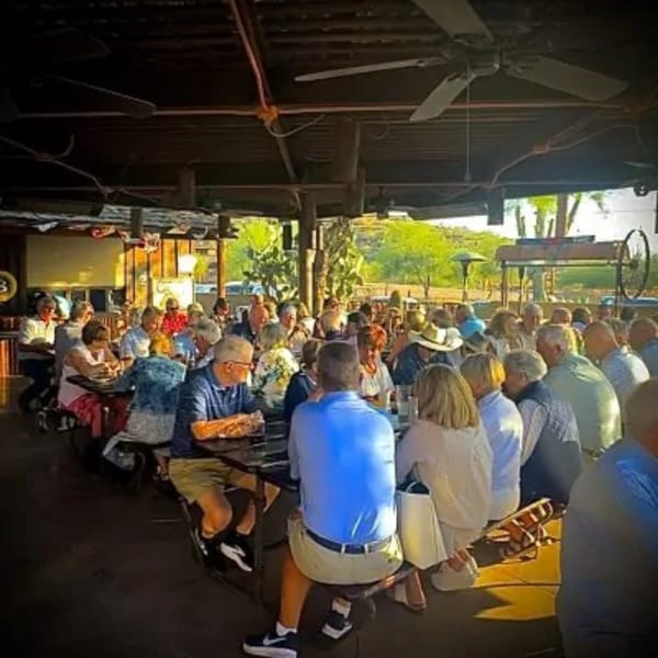 Diners seated at long tables under a covered patio, enjoying a meal at The Horny Toad restaurant.