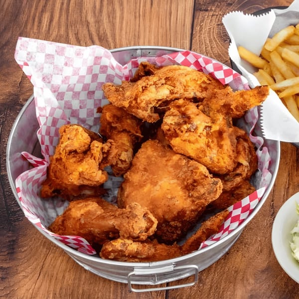 A metal bucket filled with crispy fried chicken pieces and a side of french fries.